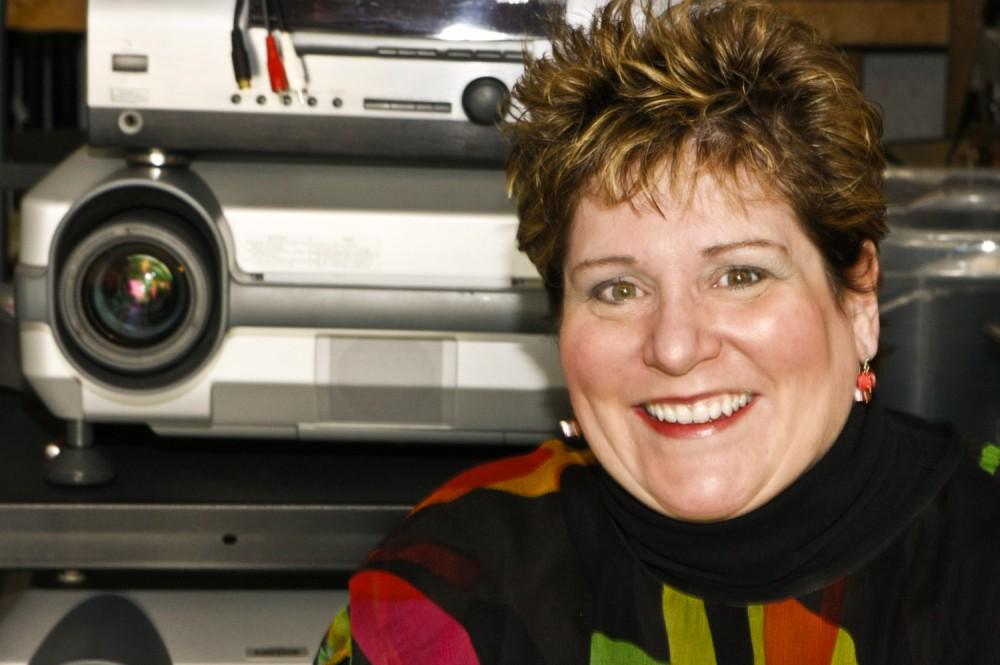 Professor Kim Roberts sits in front of her projectors, which she uses for her video installation artwork. She was the first artist at Kendall College of Art and Design to combine video and sculpture in one piece of art.