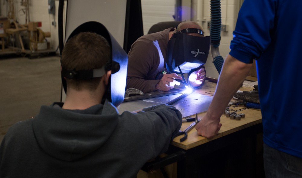 GVL / Kevin Sielaff -  Contracted welder Jake Dykstra performs the finishing touches on all of the vehicle’s a-arms as SAE member Garrett Goodwin helds hold the metal in place on Saturday, Feb. 27, 2016 inside the vehicle bay at Grand Valley’s John C. Kennedy Hall of Engineering.