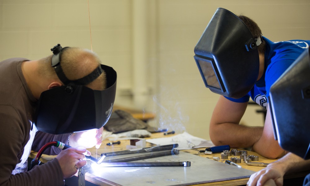 GVL / Kevin Sielaff -  Contracted welder Jake Dykstra performs the finishing touches on all of the vehicle’s a-arms as GVSU student and SAE member Bert Vossler watches on Saturday, Feb. 27, 2016 inside the vehicle bay at Grand Valley’s John C. Kennedy Hall of Engineering.