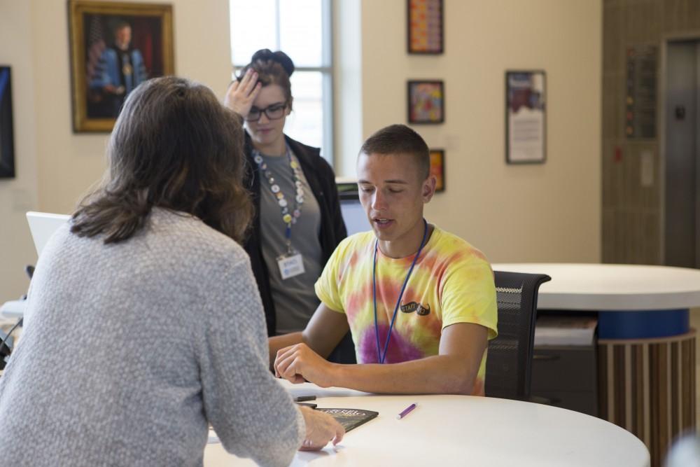 GVL / Sara Carte - Student library worker, Eli Bale (right), helps people check out books at the Mary Idema Pew Library on Allendale’s campus on Monday, Mar. 14, 2016.