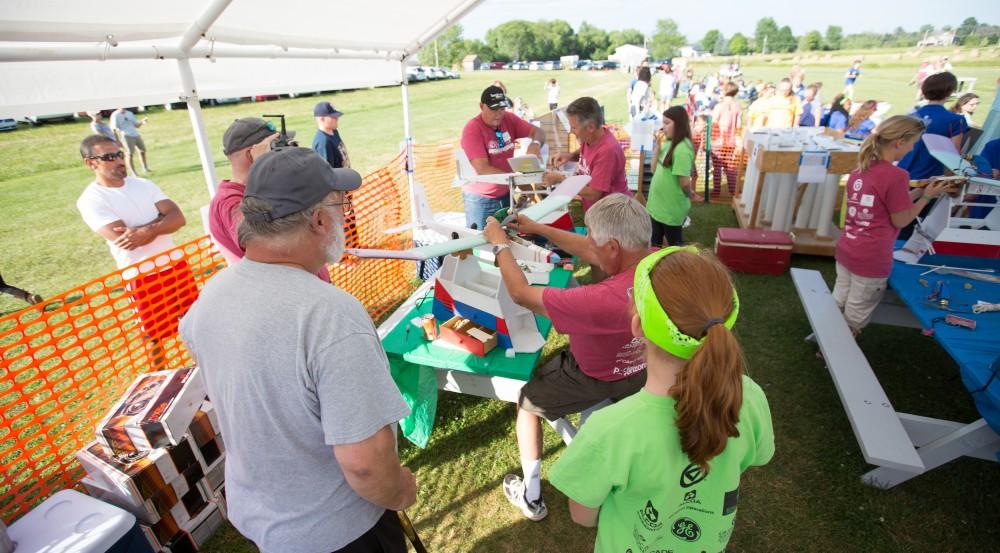 GVL / Kevin Sielaff - Volunteers help repair and assemble plane parts next to the launch site. Students of STEPS (Science, Technology, and Engineering Day Camps) fly planes that they have built during camp at Warped Wings Fly Field in Allendale on Thursday, June 23, 2016. 