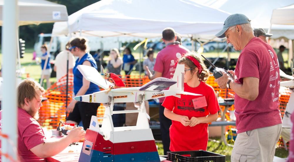 GVL / Kevin Sielaff - Volunteers help repair and assemble plane parts next to the launch site. Students of STEPS (Science, Technology, and Engineering Day Camps) fly planes that they have built during camp at Warped Wings Fly Field in Allendale on Thursday, June 23, 2016. 