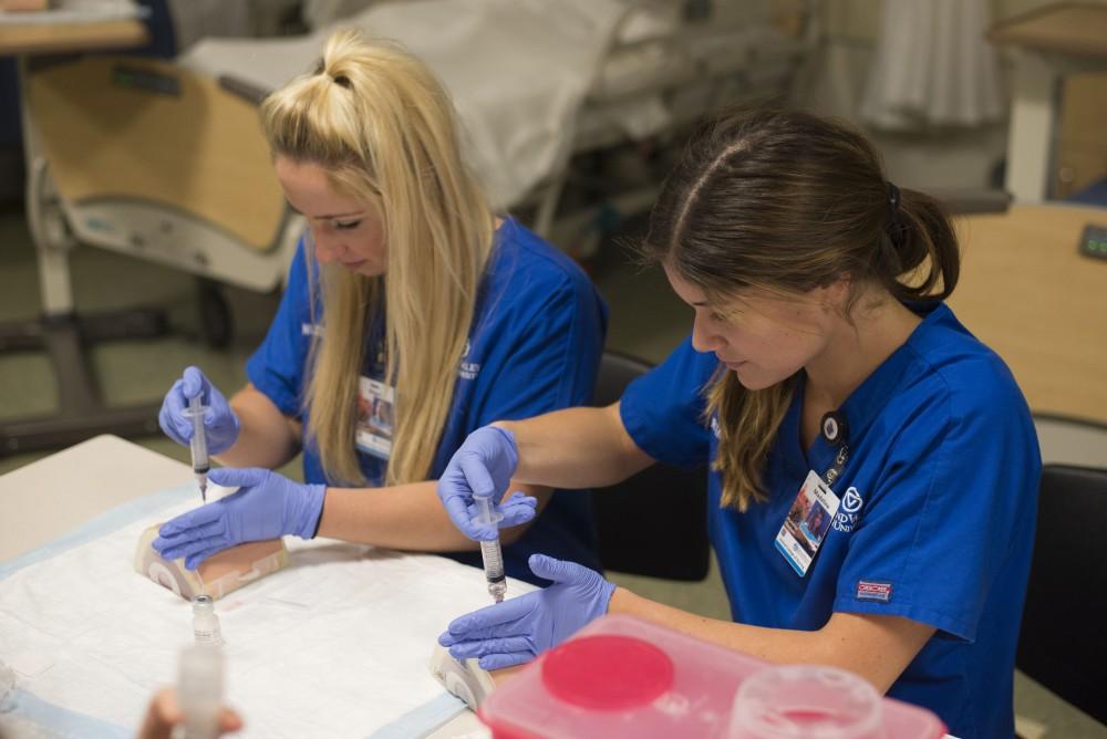 GVL / Luke Holmes - Megan Buchman (left) and Madeline Madison (right) practice giving shots to test dummies in the Center for Health Sciences building downtown.