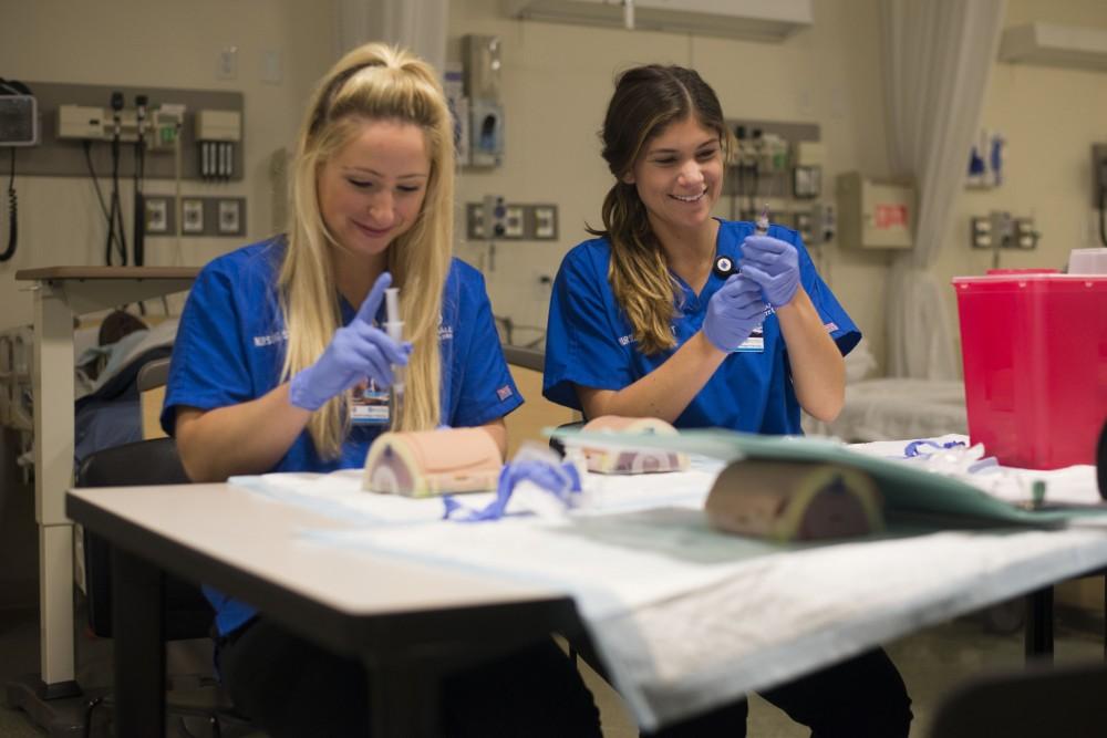 GVL / Luke Holmes - Megan Buchman (left) and Madeline Madison (right) practice giving shots to test dummies in the Center for Health Sciences building downtown.