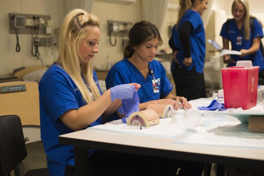 GVL / Luke Holmes - Megan Buchman (left) and Madeline Madison (right) practice giving shots to test dummies in the Center for Health Sciences building downtown.