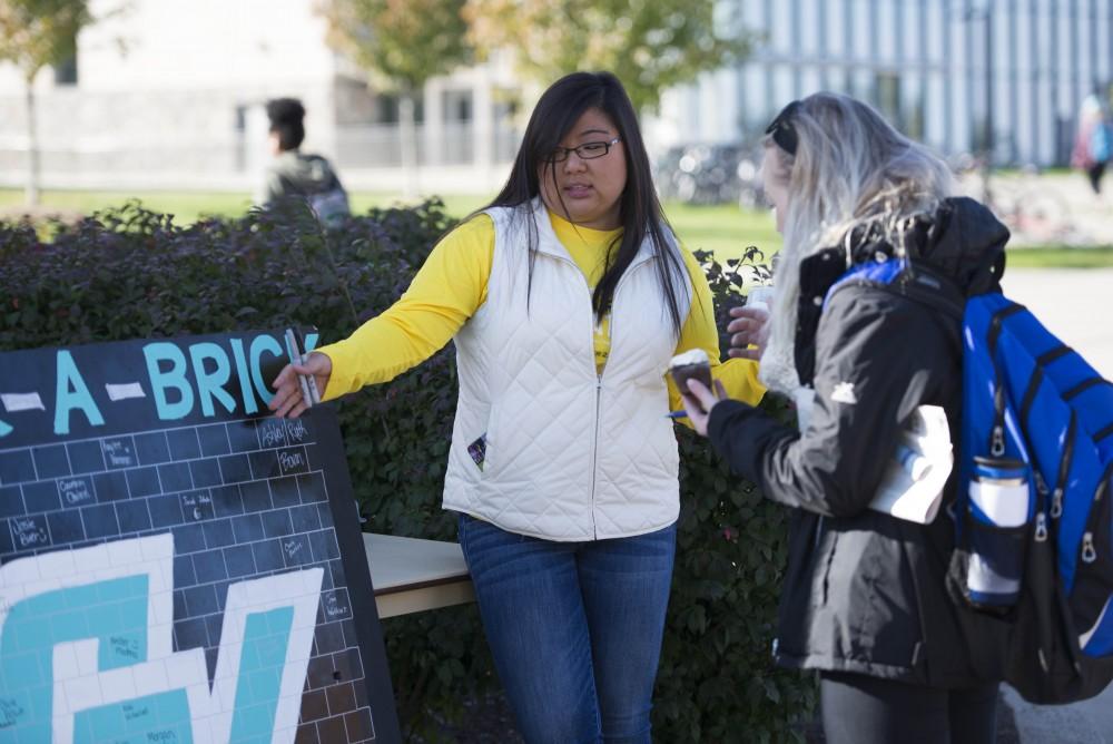 GVL / Luke Holmes - Kaylee Harmon explains the "Buck-A-Brick" board to a student. GVSU Founders Day was celebrated on Tuesday, Oct. 25, 2016 next to the clock tower.